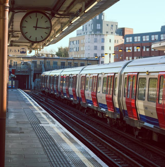 View of St Johns Wood station platform with clean, polished tiles and tactile paving along the edge, overlooking a modern London underground train with a stainless steel exterior featuring red and blu