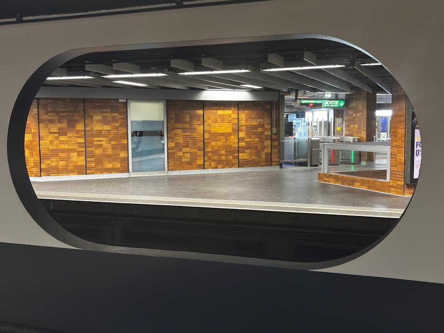 View of St Johns Wood station platform with clean, polished tiles and tactile paving along the edge, overlooking a modern London underground train with a stainless steel exterior featuring red and blu